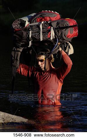 Mid adult man carrying a backpack over his head while crossing a river View Large Photo Image Stock Photo - Mid adult man carrying a backpack over his head while crossing a river. Fotosearch