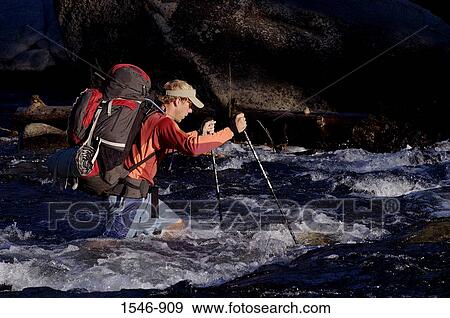 Stock Photo - Mid adult man crossing a river. Fotosearch