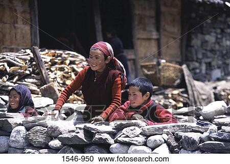 Stock Image - Two girls and a boy standing behind a stone wall, Samagaon Village, Nepal. Fotosearch