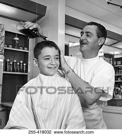 Stock Image - Barber applying cosmetics on boy's head. Fotosearch