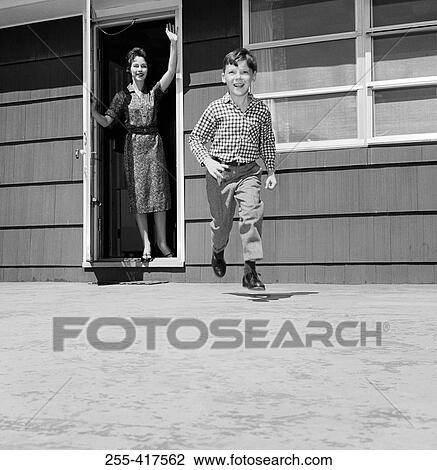 Stock Image - Boy running in backyard, mother waving. Fotosearch