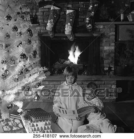 Stock Photo - Children reading book under Christmas tree. Fotosearch