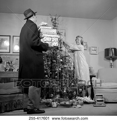 Stock Image - Couple preparing Christmas tree in living room. Fotosearch