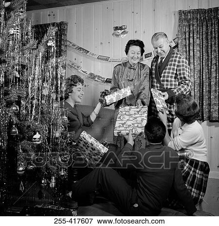 Family exchanging gifts by Christmas tree in living room View Large Photo Image Stock Photo - Family exchanging gifts by Christmas tree in living room. Fotosearch