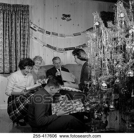 Stock Photograph - Family opening gifts by Christmas tree in living room. Fotosearch