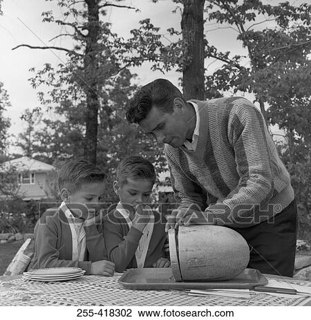 Stock Image - Father with twin sons cutting watermelon. Fotosearch