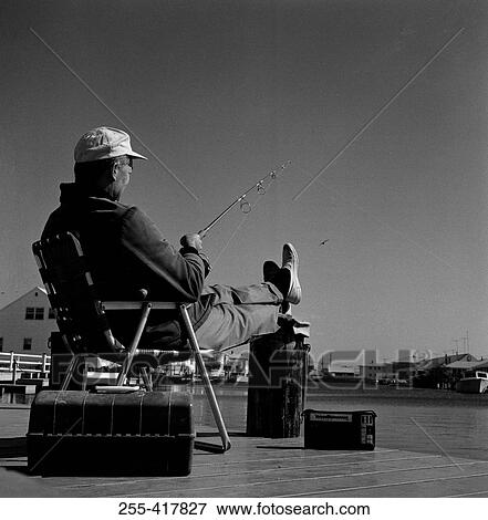 Stock Photo - Fisherman sitting in chair at the edge of water. Fotosearch