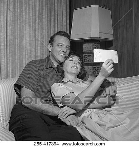 Picture - Happy couple on sofa looking at picture. Fotosearch
