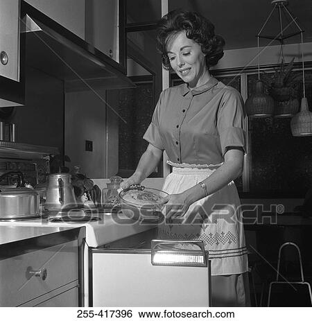 Stock Photograph - Happy woman putting meal into oven. Fotosearch
