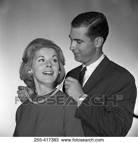 Stock Image - Man fastening to woman pearl necklace, studio shot. Fotosearch