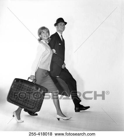 Stock Photo - Mid adult couple carrying suitcases and smiling. Fotosearch
