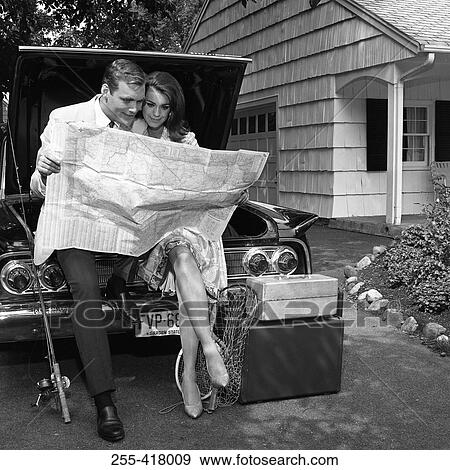 Stock Photo - Mid adult couple sitting on car and reading map. Fotosearch
