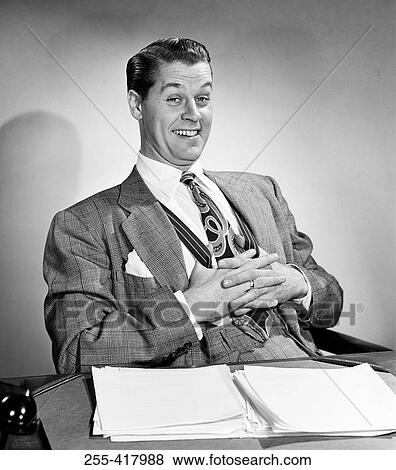 Mid adult man sitting at desk in office and smiling View Large Photo Image Stock Photo - Mid adult man sitting at desk in office and smiling. Fotosearch