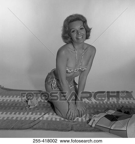 Stock Image - Mid adult woman in bikini sitting on blanket. Fotosearch