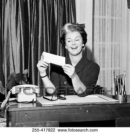 Mid adult woman sitting at desk and holding paycheck View Large Photo Image Stock Image - Mid adult woman sitting at desk and holding paycheck. Fotosearch