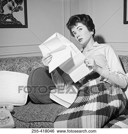 Stock Photograph - Mid adult woman sitting on sofa holding letter. Fotosearch