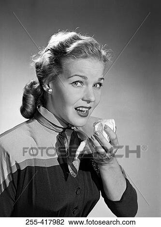 Stock Image - Mid adult woman sneezing and holding tissue. Fotosearch