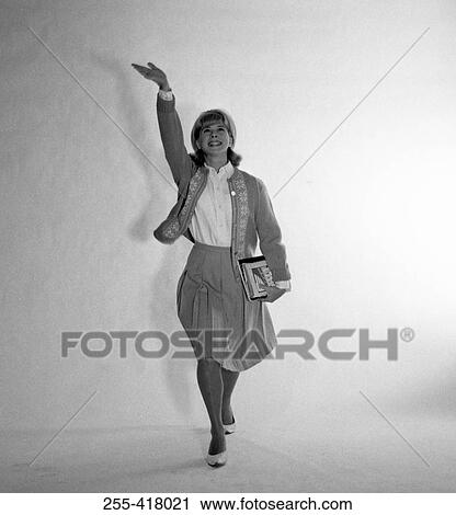 Stock Image - Mid adult woman walking with hand up. Fotosearch