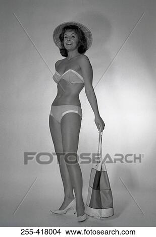 Mid adult woman wearing bikini and straw hat holding beach bag View Large Photo Image Picture - Mid adult woman wearing bikini and straw hat holding beach bag. Fotosearch