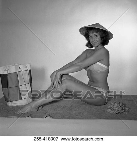 Stock Photo - Mid adult woman wearing bikini sitting on towel. Fotosearch