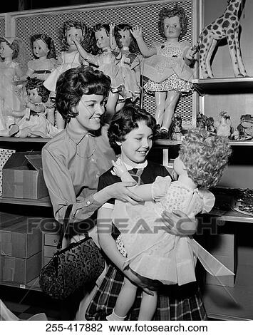 Stock Image - Mother and daughter observing doll in toy shop. Fotosearch