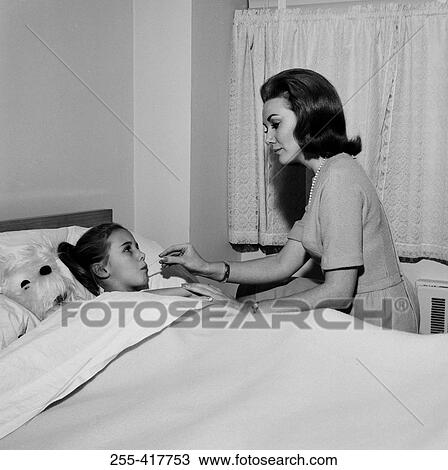 Stock Image - Mother checking daughter's temperature in bed. Fotosearch