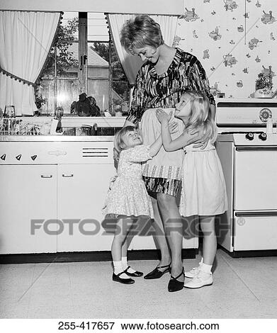 Stock Photo - Mother embracing daughters in kitchen. Fotosearch