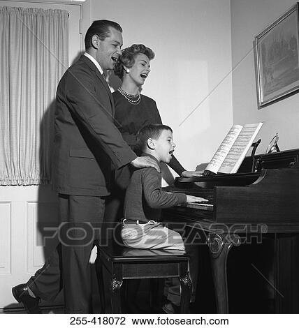 Stock Image - Parents singing with son playing piano. Fotosearch