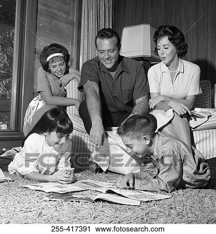 Stock Image - Parents sitting and looking at children reading on carpet. Fotosearch