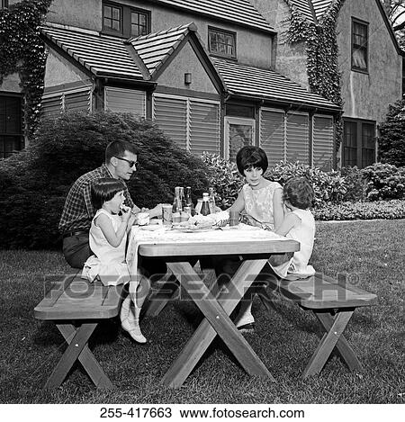 Stock Image - Parents with daughters at picnic table in garden. Fotosearch