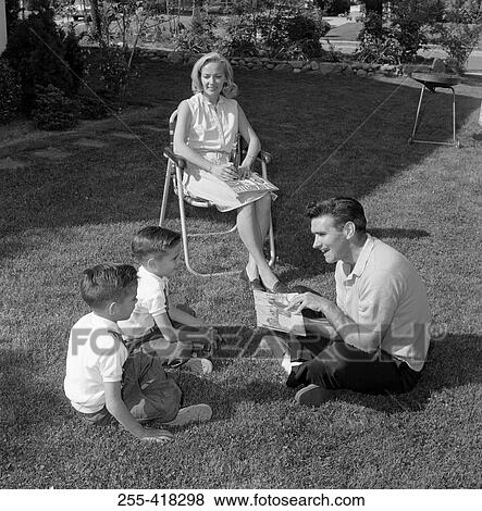 Stock Photo - Parents with twin sons reading book sitting on lawn. Fotosearch