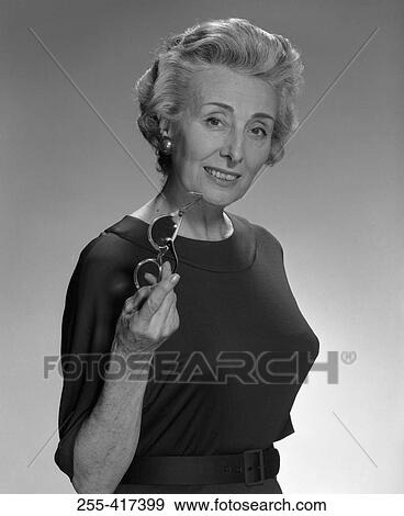 Stock Photo - Portrait of smiled old woman holding glasses, studio shot. Fotosearch