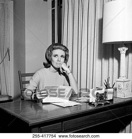 Picture - Sad young woman sitting at desk, holding letter. Fotosearch