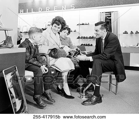 Stock Image - Shop assistant showing boy shoe to mother with son and daughter. Fotosearch
