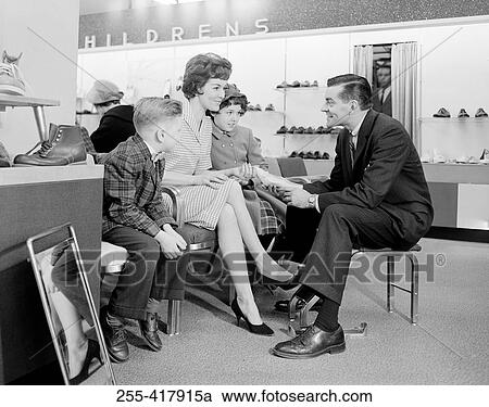 Stock Image - Shop assistant showing women's shoe to mother with son and daughter. Fotosearch