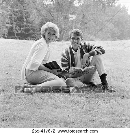 Stock Image - Student couple sitting on grass with open books. Fotosearch