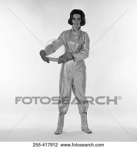 Stock Image - Studio portrait of female astronaut holding helmet. Fotosearch