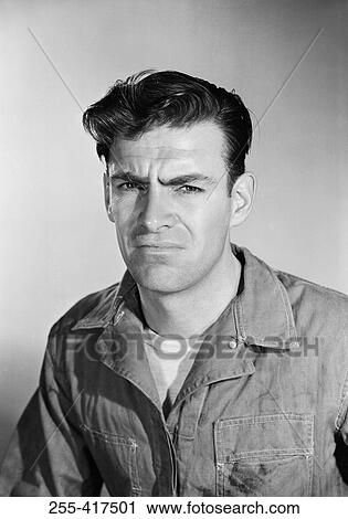 Stock Image - Studio portrait of mid adult man in coveralls. Fotosearch