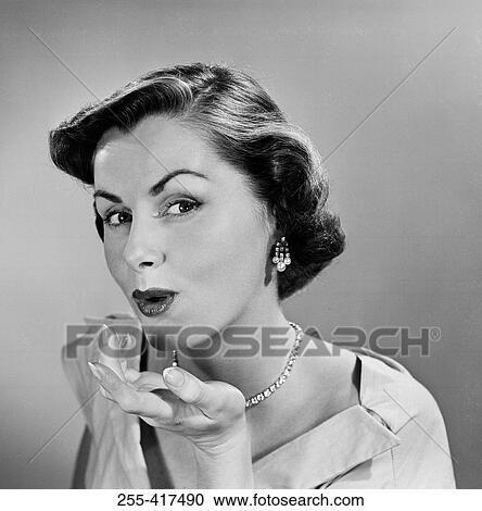 Stock Image - Studio portrait of young woman blowing kiss. Fotosearch