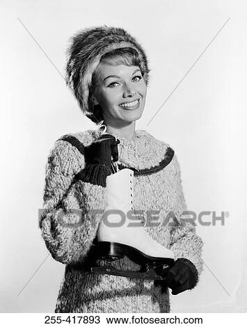 Stock Image - Studio portrait of young woman holding ice skate. Fotosearch