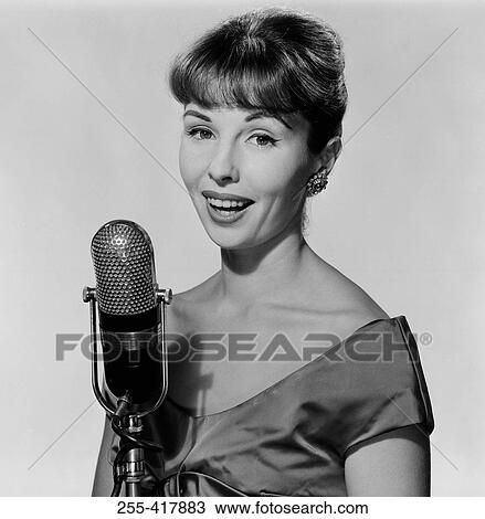 Stock Image - Studio portrait of young woman singing into microphone. Fotosearch