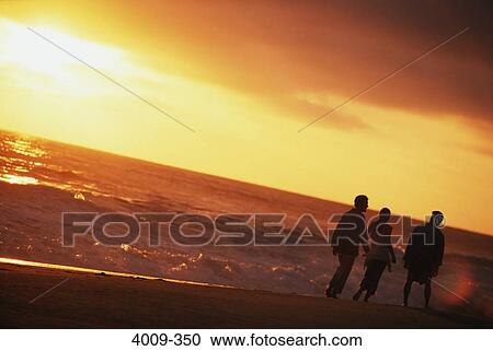 Stock Image - Three tourists walking on the beach. Fotosearch
