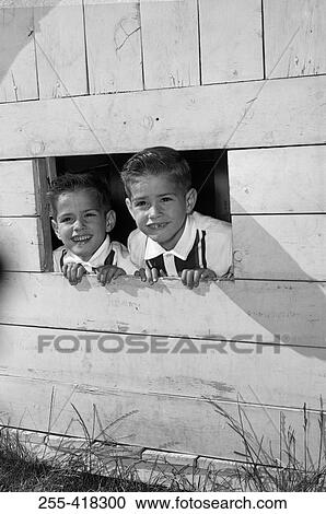 Stock Image - Twin brothers looking through window of wooden playhouse. Fotosearch