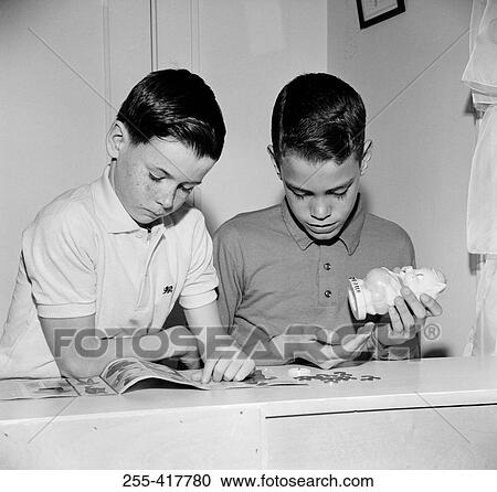 Stock Image - Two boys reading magazine and taking out money from money-box. Fotosearch