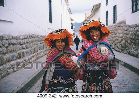 Stock Image - Two girls standing in the street holding two puppies, Cuzco, Cusco Region, Peru. Fotosearch