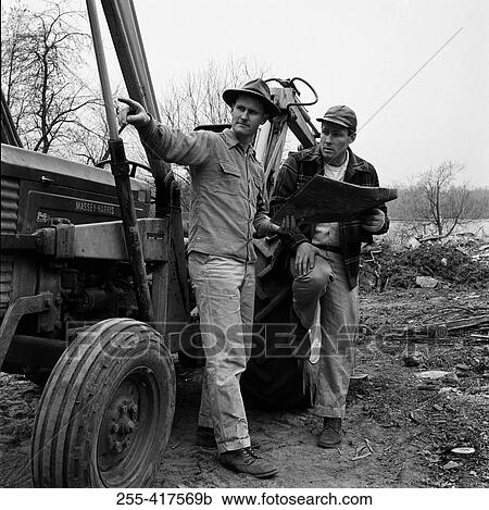 Stock Image - Two men standing by tractor discussing plans. Fotosearch