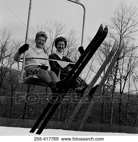 Stock Photo - Two woman sitting ski lift, looking at camera and smiling. Fotosearch