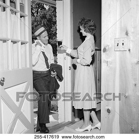 Stock Photo - Woman giving husband drink at front door. Fotosearch