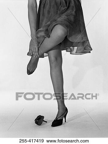 Stock Photo - Woman standing on one leg and massaging ankle, low section. Fotosearch