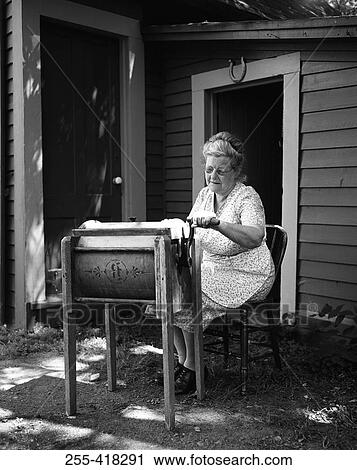 Stock Image - Woman using antique washing machine. Fotosearch